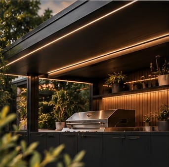 A stainless steel BBQ under a dark pod roof with warm LED strip lighting and timber-slat shelving with plants.