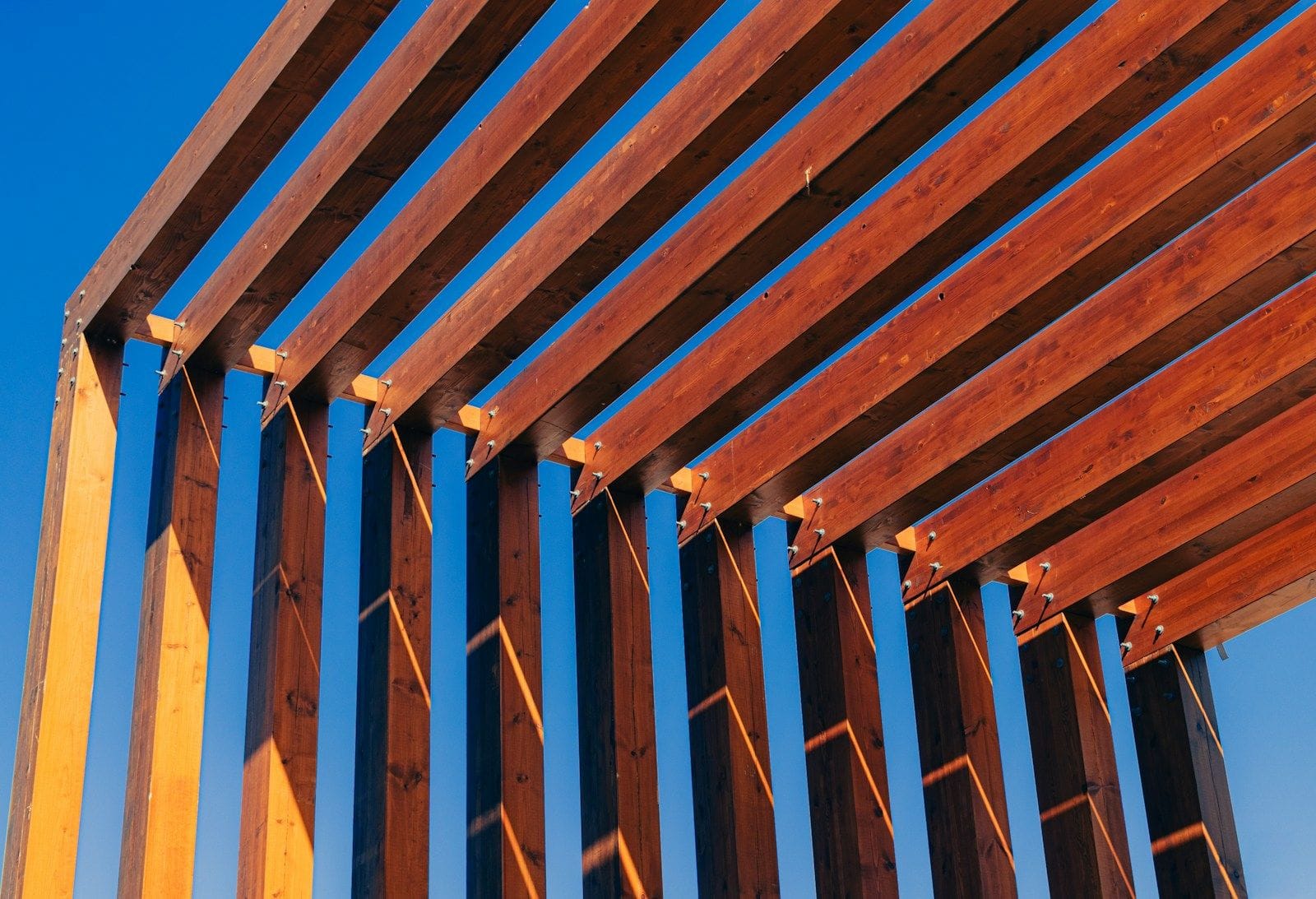 Warm timber beams of a pergola against a deep blue sky.